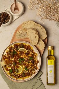 Mediterranes Gericht mit Oliven, getrockneten Tomaten und Brot, daneben eine Flasche Olivenöl extra nativ.