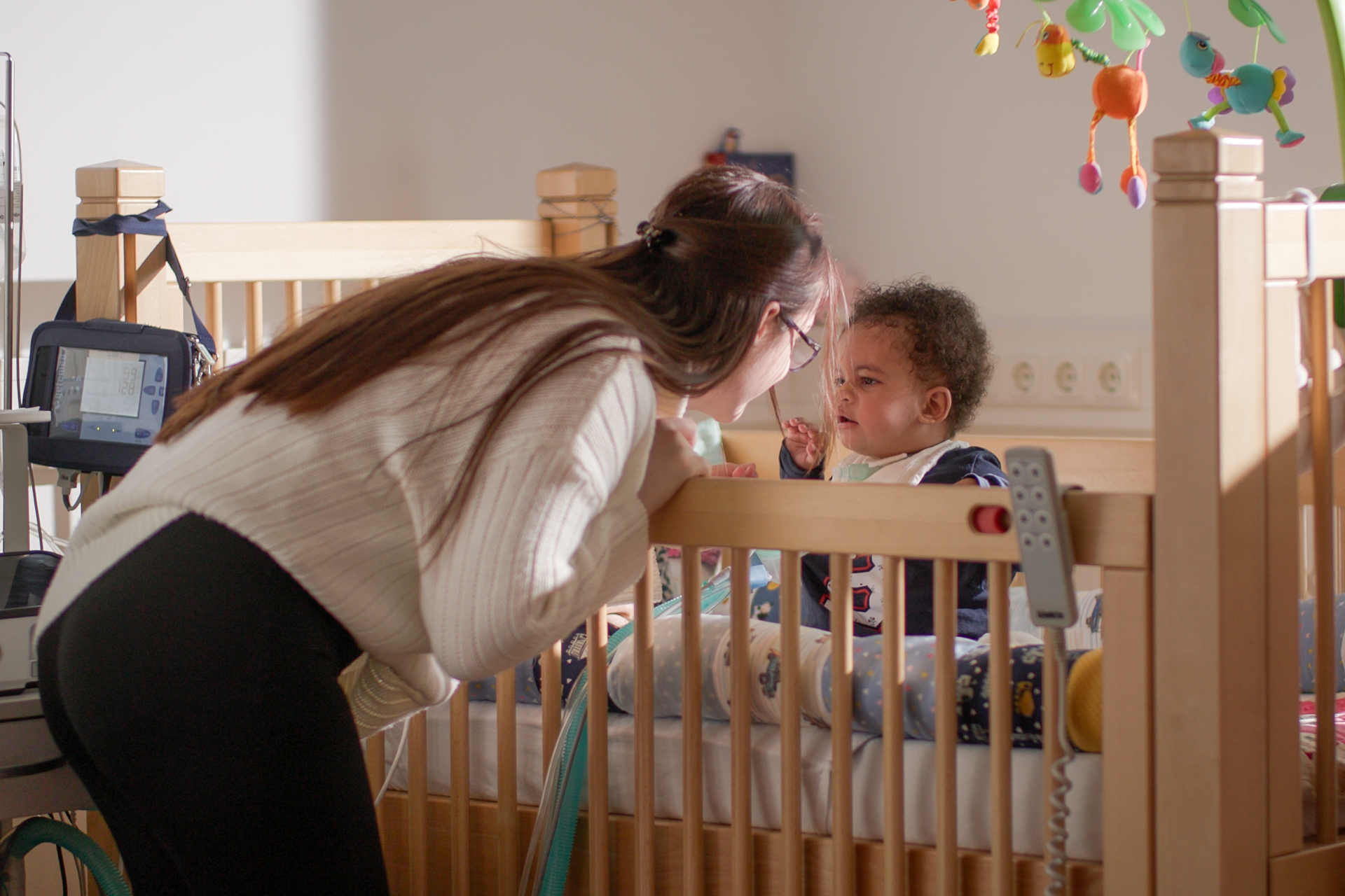 Übergangseinrichtung beatmete Kinder Deutschland Mutter beugt sich fürsorglich zu ihrem beatmeten Kleinkind im Gitterbett – Alltag mit außerklinischer Intensivpflege