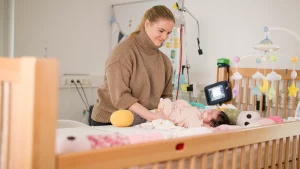 Mutter steht bei ihrem beatmeten Kind im Haus Atemzeit und kontrolliert die Beatmungsmaschine Beatmetes Kind zu Hause