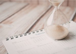 Sanduhr auf einem aufgeschlagenen Kalender auf einem hellen Holztisch Fehler bei der Altersvorsorge